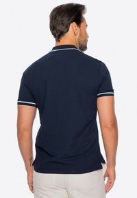 Námořnická polo košile s vroubkovanou texturou, s krátkým rukávem a bílými akcenty na límci a rukávech. Zobrazeno ze zadní strany.