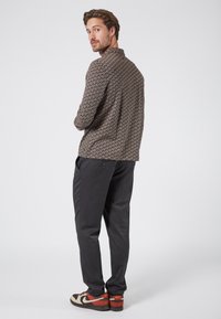 Camisa marrón con estampado, de mangas largas, pantalones negros y zapatillas marrones y rojas. La tela tiene un aspecto texturizado y un corte ajustado.