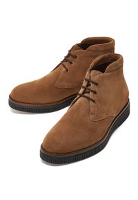 Bottines en daim marron avec semelles en caoutchouc noir et lacets marron foncé, placées côte à côte sur fond blanc.