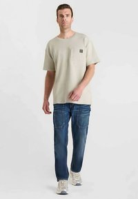 Lichtgrijs T-shirt met korte mouwen en een borstzak, gecombineerd met blauwe jeans met zichtbare stiksels en twee zijzakken.