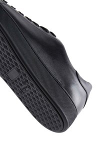 Zapatilla de cuero negro con suela de goma texturizada. Presenta un upper suave, patrón de diamante en la suela y diseño minimalista.