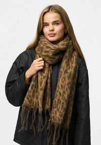 Brun leopardprint tørklæde lavet af blødt, struktureret stof med frynser i enderne, båret over en sort quilted jakke.