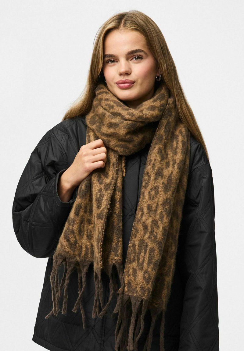 Brun leopardprint tørklæde lavet af blødt, struktureret stof med frynser i enderne, båret over en sort quilted jakke.