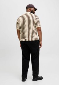 Maglietta a maniche corte in maglia color crema con righe verticali marroni; abbinata a pantaloni neri e scarpe nere; vestibilità casual.