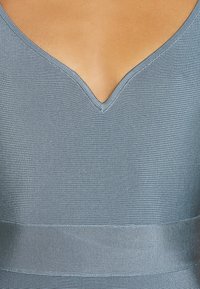 Gros plan sur une femme portant un haut bleu clair côtelé à col en V, dévoilant le haut de la poitrine et le décolleté.