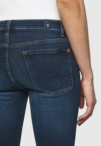 Mörkblå denimjeans med slim fit, med ett subtilt sytt mönster på bakfickorna och detaljer i kopparfärg.