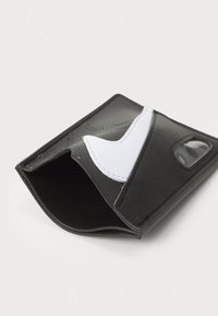 Schwarze Lederbörse mit einem weißen Nike-Swoosh-Logo, strukturiertem Oberflächen und einem transparenten Kartenfach. Kompaktes, kantiges Design.