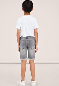 Gray denim shorts with rolled cuffs, back pockets, and a faded finish, paired with a plain white t-shirt and white sneakers.