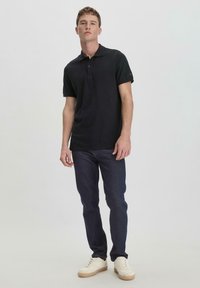 Black polo shirt with short sleeves, made of cotton, featuring a classic collar and two-button placket, paired with dark jeans and white sneakers.