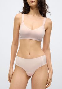 Σετ ελαφρώς ροζ εσώρουχα με απαλή, λεία υφή. Το σουτιέν έχει λεπτές τιράντες και στρογγυλεμένο ντεκολτέ, ενώ το εσώρουχο είναι στυλ hipster.