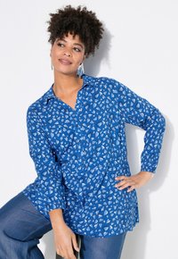 Blå långärmad skjorta med ett mönster av ljusblå hjärtan, en notch-krage och elastiska ärmslut, tillsammans med denimbyxor.