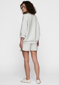 Felpa grigia chiaro con vestibilità ampia e maniche arrotolate, abbinata a pantaloni corti coordinati. Presenta una texture liscia e un design casual.