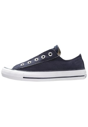 Navy blauwe lage sneaker van canvas zonder veters, met een witte rubberen zool en metalen veteroogjes, op een witte achtergrond.