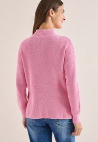 Maglione rosa a coste con collo alto e maniche lunghe, caratterizzato da un fit rilassato e un tessuto testurizzato. Abbinato a jeans blu.