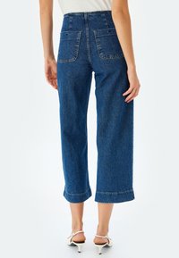 Culottes de mezclilla azul de talle alto con puños enrollados, que cuentan con dos bolsillos traseros y un acabado texturizado. Detalle de costura estándar en toda la prenda.