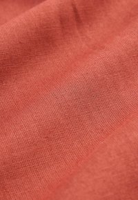 Gros plan sur un tissu doux et tissé de couleur terre cuite pâle, montrant une texture détaillée et des plis subtils.