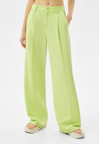 Pantalons larges vert clair avec des plis, en tissu lisse. Comprend des poches latérales et une fermeture à un bouton au niveau de la taille.