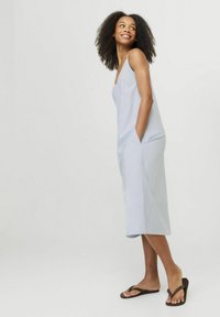 Vestido midi a rayas de color azul claro con escote en V y bolsillos; tejido suave y corte recto. Llevado con chanclas marrones.