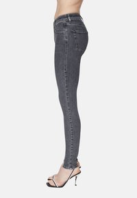 Jeans skinny grises con una cintura alta, diseño de cinco bolsillos y detalles de costura mínimos. Llevados con tacones altos negros con tiras.