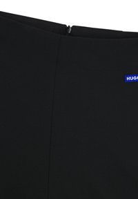 Černé šaty s hladkou, strukturovanou tkaninou. Mají zip na zádech a modrou vyšívanou nášivku na boku. Minimalistický design.