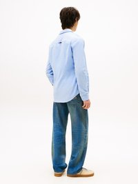 Camisa de manga larga azul claro con cuello, combinada con jeans de corte holgado azul y zapatillas beige. Presenta costuras sutiles y detalles en la parte trasera.