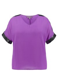 Lila kortärmad topp med V-ringning, prydd med svarta paljetter på ärmarna. Tillverkad av mjukt material med en avslappnad passform.