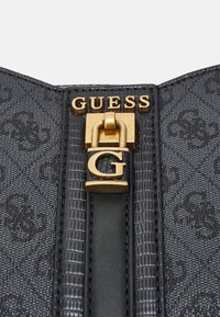 Musta kuvioitu käsilaukku, jossa on tekstuuripinta, ja joka sisältää kultasävyisiä varusteita sekä lukon, jossa on "G"-logo.