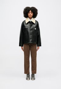 Czarna skórzana kurtka z kremowym futrzanym kołnierzem, zapinana na guziki, z dwiema przednimi kieszeniami, w zestawie z brązowymi spodniami i szarymi butami.