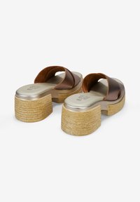 Sandalias de piel marrón con una tira ancha, suela metálica dorada y un tacón de plataforma de yute texturizado. Plantilla lisa con detalles de marca.