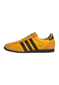 Gula Adidas Japan-sneakers med svarta ränder, perforerad tå, detaljer i mocka och svart sula, visad från sidan mot en vit bakgrund.
