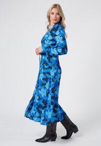 Niebieska kwiecista sukienka maxi z długimi rękawami, ściągnięta w talii, o gładkiej fakturze materiału. W zestawie z czarnymi kowbojkami.