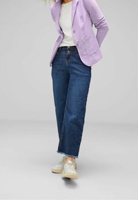 Světlý fialový blazer, bílá košile, tmavě modré džíny s vysokým pasem a roztrhaným lemem, a světlé tenisky. Hladké látky s uvolněným střihem.