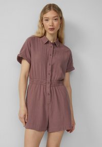 Kurzärmliger, kragenloser Jumpsuit in stäubenem Rosé. Texturiertes, leichtes Material mit Knöpfen an der Vorderseite und einem elastischen Bund für eine gute Passform.