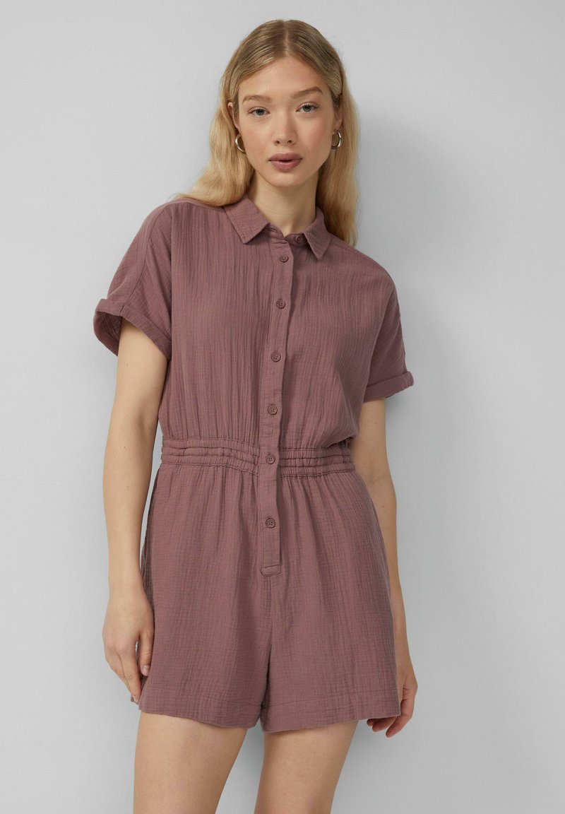 Kurzärmliger, kragenloser Jumpsuit in stäubenem Rosé. Texturiertes, leichtes Material mit Knöpfen an der Vorderseite und einem elastischen Bund für eine gute Passform.