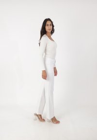 Ideal blanco de manga larga combinado con jeans acampanados blancos de cintura alta, con aberturas laterales. Sandalias de tacón transparente completan el atuendo.