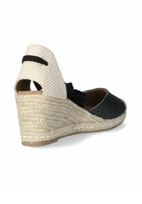 Espadrille de cuña en negro y beige con suela de yute trenzado. La parte trasera presenta una tela a cuadros y un detalle de lazo negro en el tobillo.