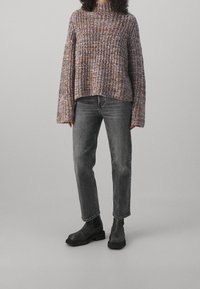 Suéter de punto en tonos morados, naranjas y crema; corte holgado con cuello alto. Combinado con jeans grises y botines negros.
