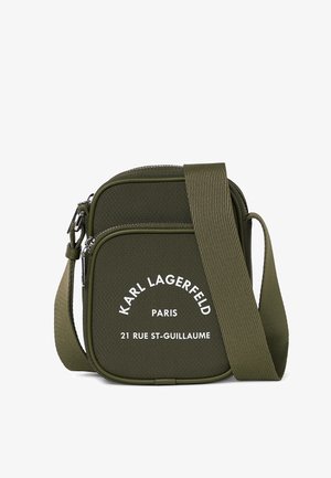 Oliwkowa torebka na ramię o teksturowanym wykończeniu, z białym logo, zapięciem na zamek i regulowanym paskiem. Kompaktowy design.