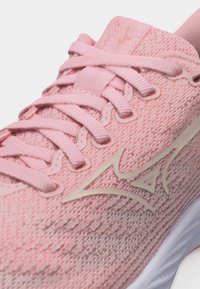 Close-up of a pink knitted running shoe with matching pink laces and a cream-colored Mizuno logo on the side.
