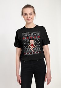 Svart t-shirt med ett rött och vitt motiv av Betty Boop, omgiven av snöflingor och hjärtan i en jultröjemönster.