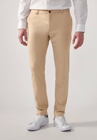 Beige trousers with a slim fit, featuring a front button closure, belt loops, and side pockets, paired with white athletic shoes.