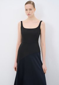 Schwarzes Kleid mit einem quadratischen Ausschnitt, tailliertem Oberteil und fließendem marineblauen Rock. Glattes Gewebe sorgt für einen Kontrast zwischen dem Ober- und dem Unterteil.