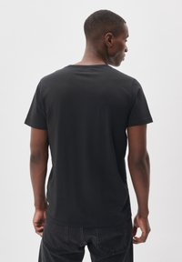 Maglietta nera in cotone con scollatura rotonda e maniche corte, caratterizzata da un design semplice e una texture liscia, vista da dietro.