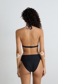 Black bikini set featuring a halter neck top and high-waisted bottom, made from smooth fabric with a minimalistic design and sleek finishes.