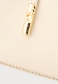 Bēša ādas soma ar reljefa apdari un zelta toņa aizdari ar ģeometrisku dizainu. Iekļautas smalkas šuvju detaļas.