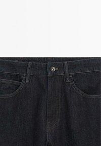 Dark denim jeans with a conventional waistband, metal button closure, and contrast stitching. Features front pockets and a textured surface.