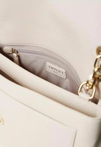 Borsa a mano in pelle crema con superficie texturizzata, metalleria dorata e una tasca con zip all'interno. L'etichetta riporta "TWINSET MILANO."
