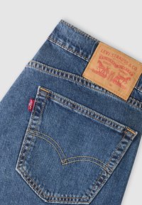 Žep na modrih denim jeans hlačah z oranžno šivom, rdečo Levi's etiketo in svetlo rjavim usnjenim znakom blagovne znamke Levi Strauss & Co. na pasu.