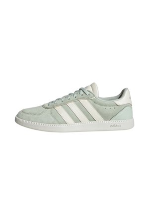 Zapatilla Adidas de ante verde claro con franjas blancas, diseño con cordones y suela de goma de marca, mostrada en perfil lateral sobre fondo blanco.