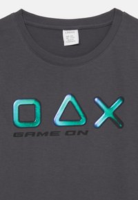 Graues Baumwoll-T-Shirt mit stilisierten Gaming-Symbolen in Türkis und Schwarz sowie dem Text "GAME ON" darunter. Klassisches Crew-Neck-Design.